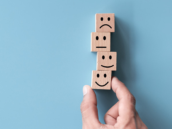 A hand holding a tower of blocks. The blocks have either sad or smiley faces on them.